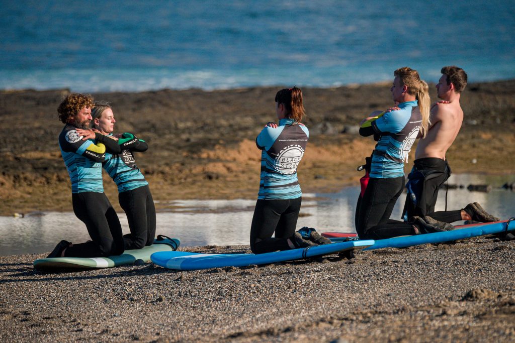Blackstone Surf Center intermediate group stretching in Playa las Américas in Tenerife before a surf course